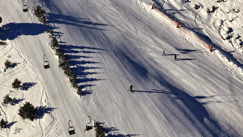 Aerial footage of skiers and snowboarders gliding down a snowy mountain slope, showcasing smooth winter sports action on a wide, sunlit piste.