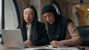 Two business women diversity girls team together in office using laptop communicate indoors multiracial females businesswomen Asian boss woman helping with software to Muslim intern writing notes - Powered by Shutterstock - Get 15% off with code: PIKWIZARD15