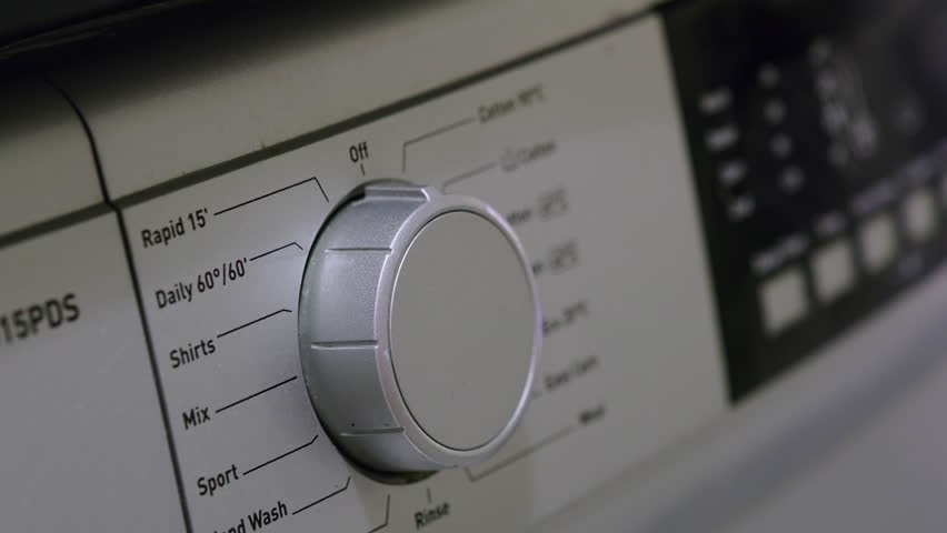 Close-up of hand turning dial and selecting washing mode on washing machine. Daily household routine