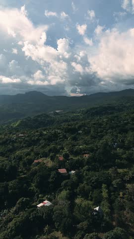 The sky is cloudy and the mountains are in the background. The trees are lush and green, and there are houses in the distance