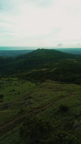 A mountain range with a green hillside and a clear blue sky. The sky is cloudy and the hillside is lush with trees