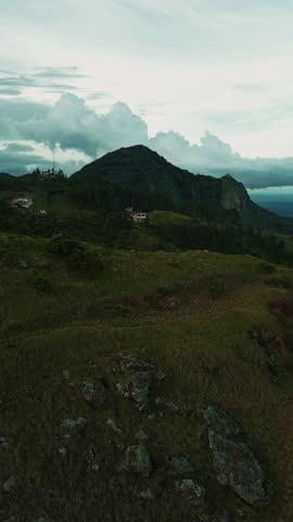 A mountain range with a house in the distance. The sky is cloudy and the grass is green