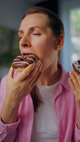 Woman with eating disorder eating two donuts with pleasure and at the same time