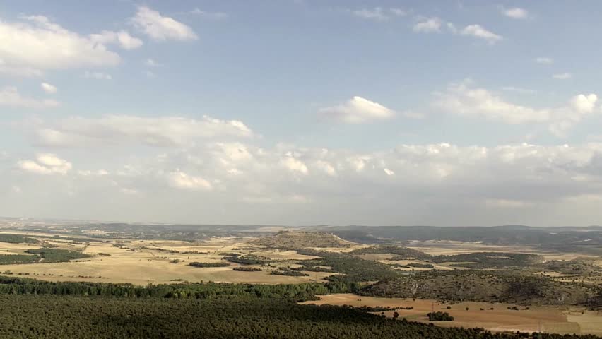 Expansive view of rolling hills and plains under a bright sky with scattered clouds