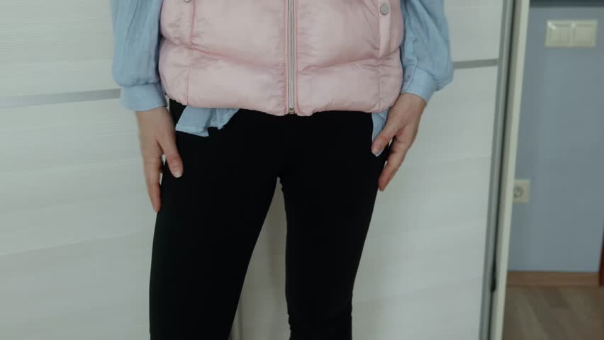 Woman in pink quilted vest, blue shirt and black pants rhythmically patting both thighs with open palms indoors.