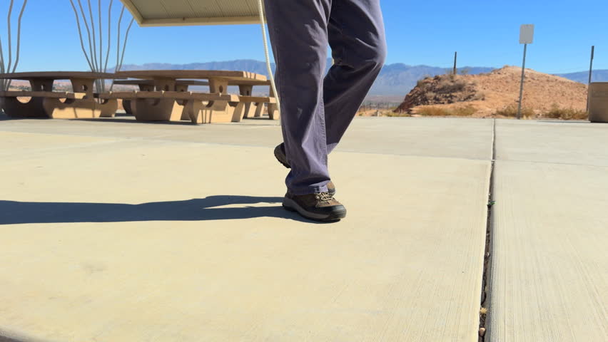 Slow motion smooth gimbal low closeup man sneaker shoe walking front view on desert sidewalk