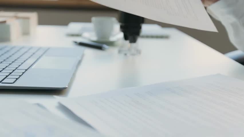 Close-up of the hands of an anonymous female secretary or paralegal reviewing an agreement and stamping official documents with a company seal while working at an office desk.