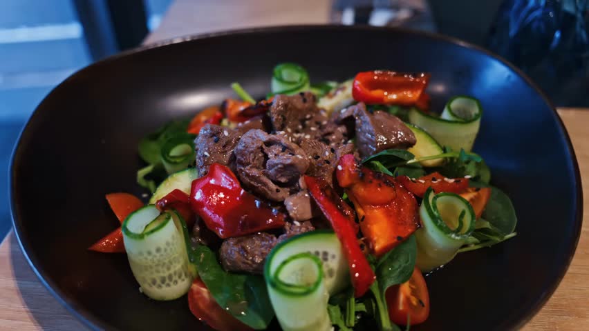 Close-up of a fresh salad with meat and vegetables on a black plate at a restaurant, highlighting healthy cuisine and gourmet presentation.