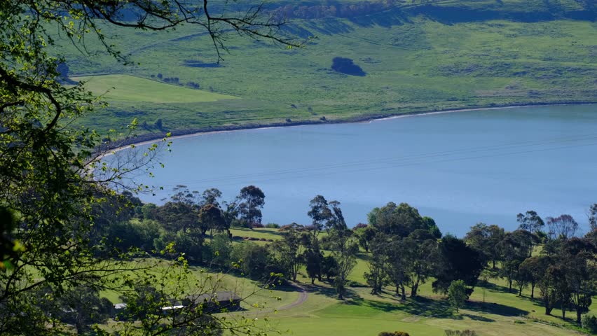  A scenic view of Lake Gnotuk near Camperdown in Victoria, Australia, showing calm blue water surrounded by rolling green farmland. A volcanic crater lake at the Western Victorian Volcanic Plains