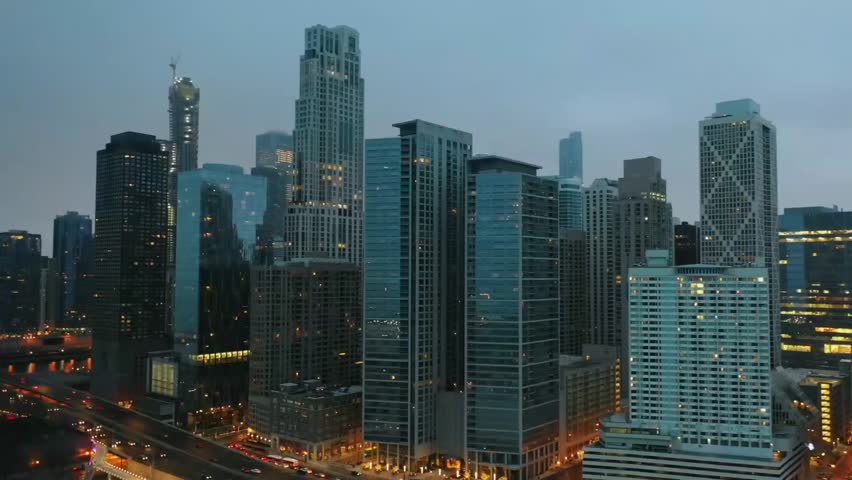 Aerial view of modern city skyline at dawn with tall towers under soft blue light.
