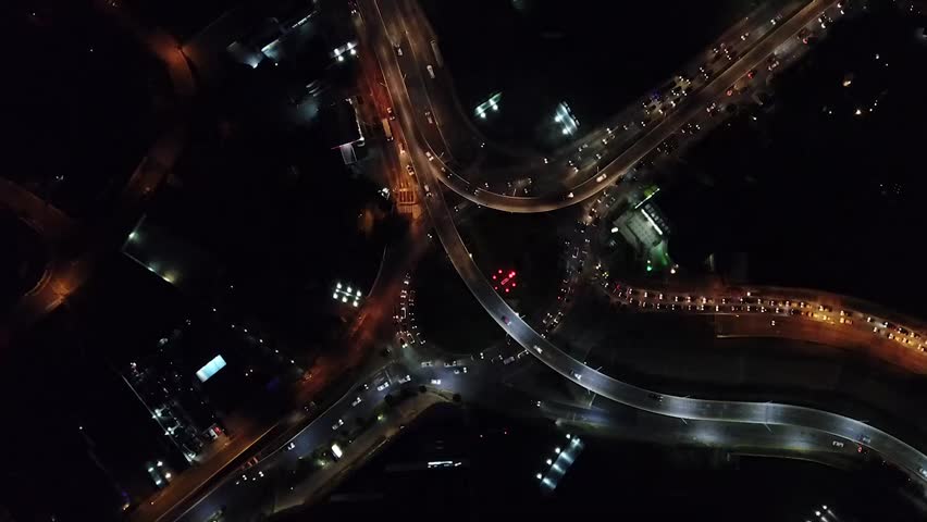 Aerial view of busy city traffic at night with glowing lights and highways.
