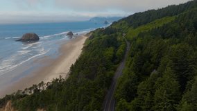 Cinematic aerial over the road at Arcadia Beach on the Oregon Coast with fir trees, sea stacks, gentle waves, cars below, and wispy low clouds drifting under a blue sky with Cannon Beach on horizon. - Powered by Shutterstock - Get 15% off with code: PIKWIZARD15