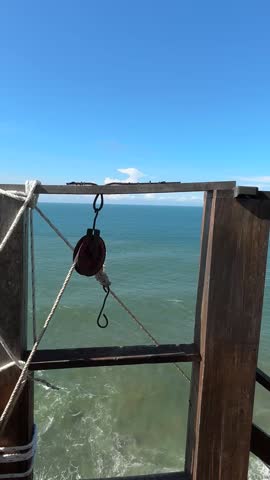 Panoramic shot of the beautiful Indian Ocean meeting a dramatic cliff at Puncak Segoro, Yogyakarta. Features a tiered wooden structure with a roof, accessible via stairs, providing a scenic dining.