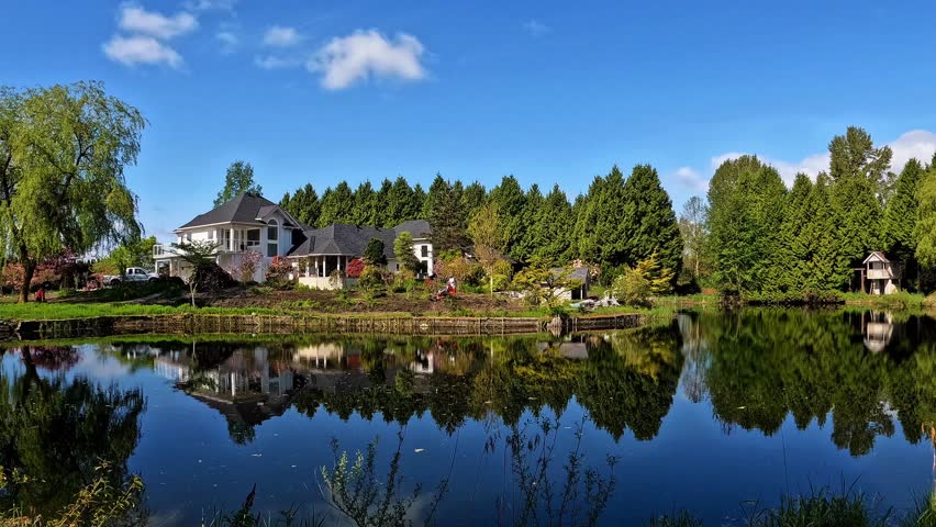 An excavator working in the backyard of a beautiful lakeside house, leveling the landscape for garden construction under clear blue sky. Peaceful waterfront property development scene.