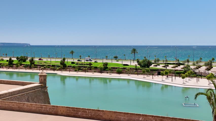Parc de la Mar with its large saltwater lake in front of the ancient city walls, with the Mediterranean Sea and a coastal road with traffic in the background on a sunny day in Palma de Mallorca