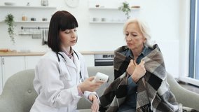 A female doctor uses a contactless thermometer to check the temperature of an elderly woman. The patient is wrapped in a blanket. - Powered by Shutterstock - Get 15% off with code: PIKWIZARD15
