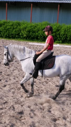 Boy rider, jockey riding on thoroughbred beautiful white stallion, horse, on the training sand field, ground. boy learns to ride a horse in horse riding school. Summer, outdoors