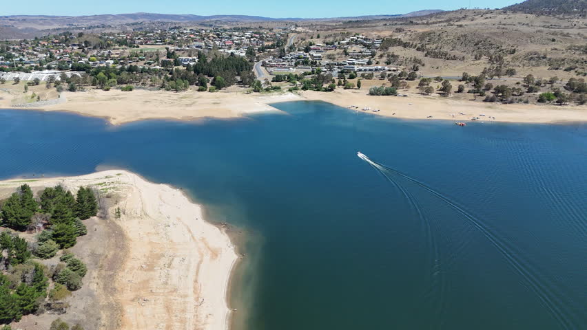 aerial drone shot of a speed boat pulling person on water ski across lake Jindabyne, an artificial body of water in the Australian Alps, part of the great dividing range and popular travel destination