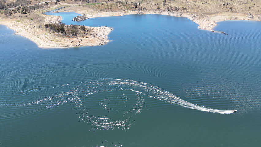 aerial drone shot of a speed boat pulling person on water ski across lake Jindabyne, an artificial body of water in the Australian Alps, part of the great dividing range and popular travel destination