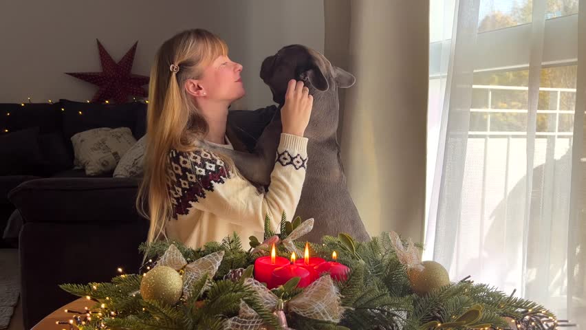 Woman in a Christmas sweater hugging a French bulldog by an Advent wreath with candles, cozy festive atmosphere, holiday with a pet