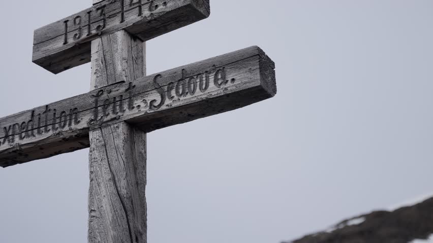 Weathered double-barred wooden memorial cross with carved inscription and 1913 14 dates, standing on a barren hillside beneath an overcast sky, signifying remembrance.