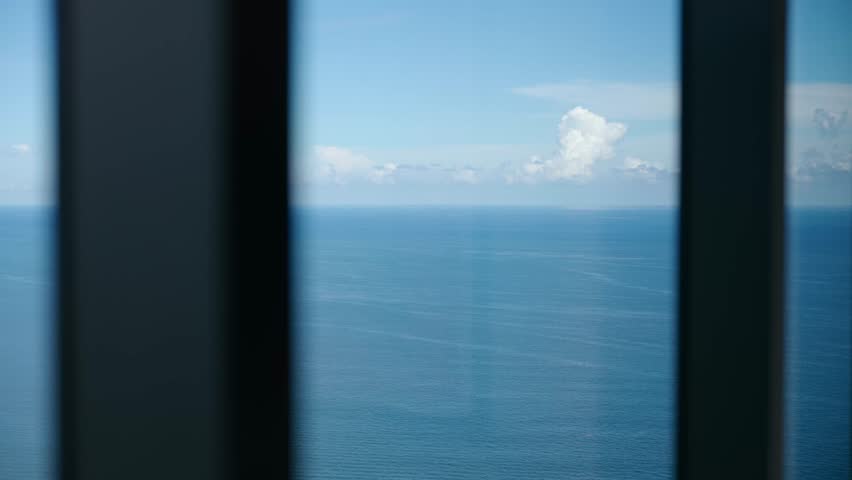 Blue ocean rests under soft clouds, seen through tall bars. Calm water and clear sky feel peaceful. Lines in front add quiet rhythm to wide, open view.