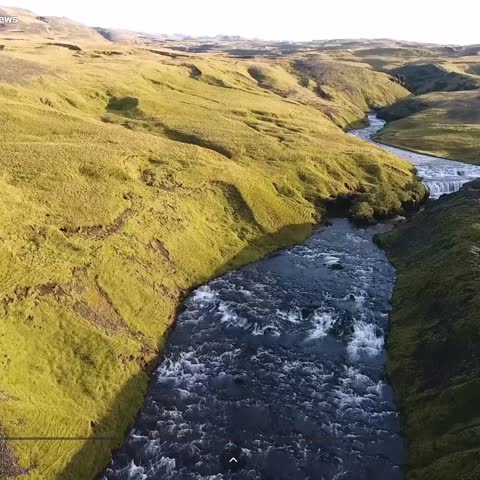 "An aerial view of a vibrant blue river winding through vast, rugged terrain covered in yellow-green grasses, emphasizing a remote natural landscape."