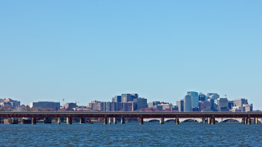 A Washington D.C. Metro train crosses the Potomac River, traveling from Virginia into DC. The skyline of Rosslyn, Virginia, is seen in the background on a clear, sunny autumn day.