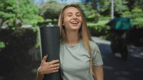 Woman smiling with a yoga mat in a lush green park setting, showcasing relaxation and happiness surrounded by nature's beauty during an outdoor fitness session. - Powered by Shutterstock - Get 15% off with code: PIKWIZARD15