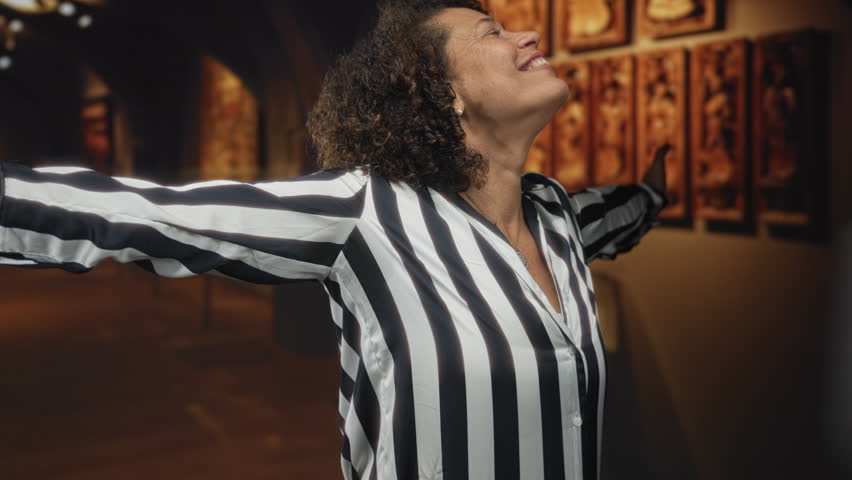 Woman wearing striped blouse smiles at grand abstract oil painting in building; cultural inspiration artistic wonder.