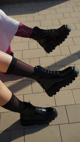 Two womens boots and shadows on sunlit pavement