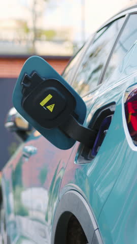 Close-up of female hands connecting an electric car charger to her vehicle outdoors.