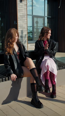 Two women in black boots sitting outdoors on bench