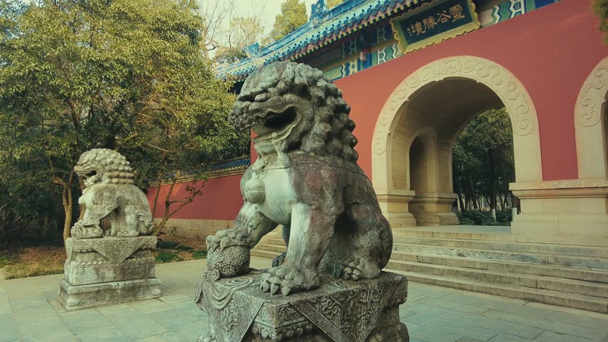 Nanjing, China. A stone lion statue in front of a red and blue building with ornate architectural details.