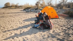 Man and woman sitting on sandy beach near a camping tent, drinking tea from thermos cups. Cozy outdoor scene with patterned blanket, warm clothes and travel mood. - Powered by Shutterstock - Get 15% off with code: PIKWIZARD15