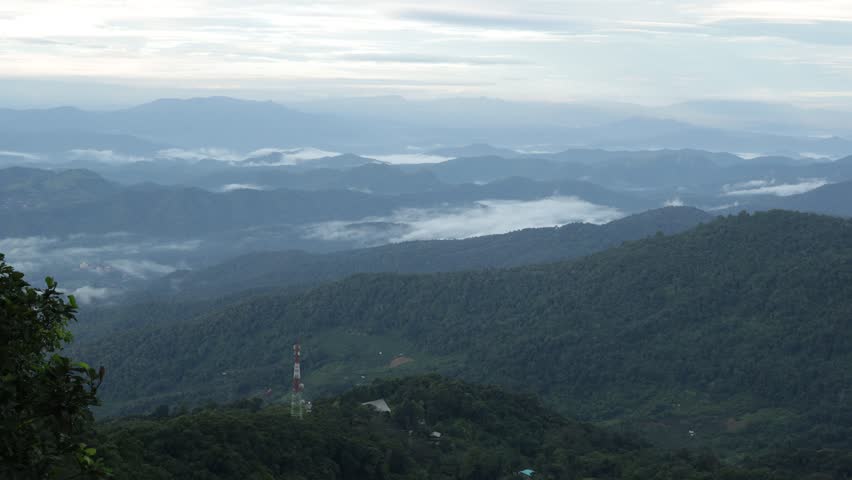 The sun was shining on the mountain, and there was a large red and white telephone pole in the middle