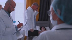 Group of doctors in white coats and masks visiting patient in hospital bed, holding tablets and clipboards, discussing diagnosis and treatment plan during medical round. - Powered by Shutterstock - Get 15% off with code: PIKWIZARD15