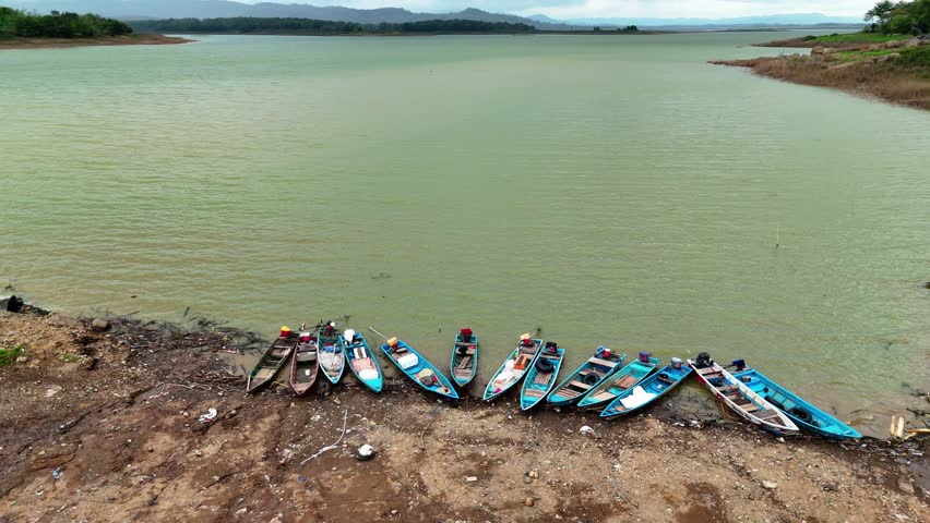 A collection of kayaks and canoes are neatly arranged on the muddy bank of a serene lake, awaiting exploration.