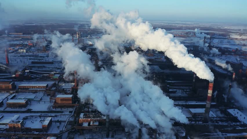 An aerial shot showcases an industrial complex with smoke stacks releasing plumes into the sky. The scene is set on a cold day, highlighting environmental concerns.