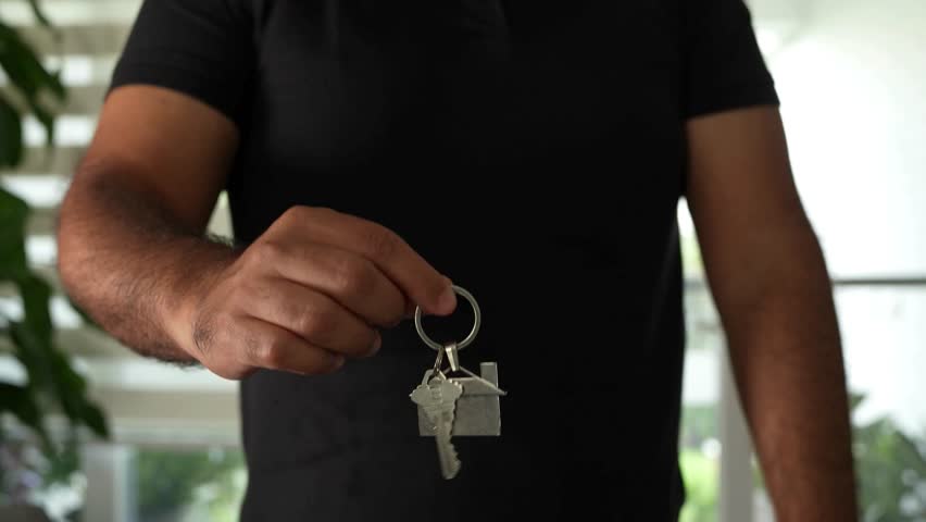 A person is holding keys with a house keychain. The background is blurred, suggesting an indoor setting. The lighting is bright, indicating it is daytime. This could be a real estate deal. - Powered by Shutterstock - Get 15% off with code: PIKWIZARD15
