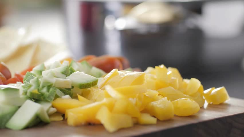 A vibrant close up showcases chopped yellow peppers, tomatoes, and other vegetables on a wooden cutting board, ready for cooking a fresh and healthy meal.