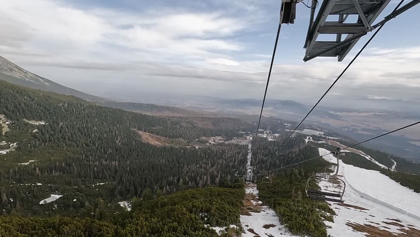 A view from an open ski lift descending the mountain. The lift seats move against the backdrop of the mountain slopes next to the ski trail. Tatra Mountains, Slovakia.