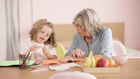 Loving grandmother teaching her cute little granddaughter how to draw while sitting at a table at home. Happy multi-generational family bonding - Powered by Shutterstock - Get 15% off with code: PIKWIZARD15