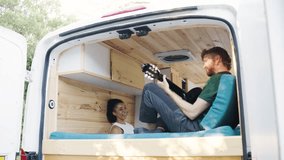 Young man serenading his girlfriend with a guitar inside their cozy, custom-built camper van. Happy couple enjoying van life and music together - Powered by Shutterstock - Get 15% off with code: PIKWIZARD15