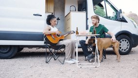 Happy diverse couple with their dog relaxing together on a road trip. Young woman playing the acoustic guitar for her partner outdoors next to their campervan - Powered by Shutterstock - Get 15% off with code: PIKWIZARD15