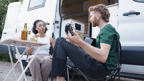 Young man playing the guitar for his girlfriend while sitting outside their camper van. Happy couple relaxing on a camping trip - Powered by Shutterstock - Get 15% off with code: PIKWIZARD15