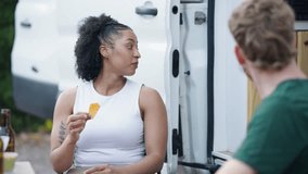 Young diverse couple enjoying a moment of connection, laughing and eating snacks together next to their camper van on a road trip getaway - Powered by Shutterstock - Get 15% off with code: PIKWIZARD15