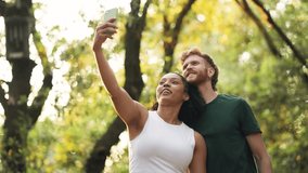 Joyful young multiracial couple smiling and taking a selfie with a smartphone outdoors. They are enjoying a beautiful day in a forest - Powered by Shutterstock - Get 15% off with code: PIKWIZARD15