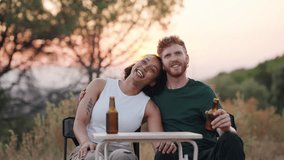 Young diverse couple enjoying a romantic outdoor date. Happy man and woman drinking beer, smiling and talking while camping at sunset - Powered by Shutterstock - Get 15% off with code: PIKWIZARD15