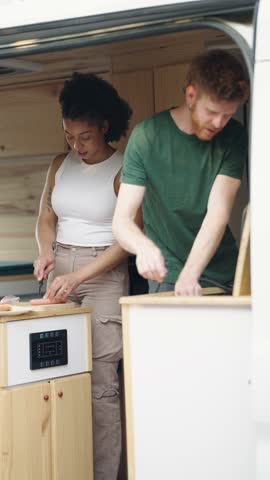 Happy interracial couple cooking together in their modern, self-converted camper van. Van life and minimalist lifestyle concept